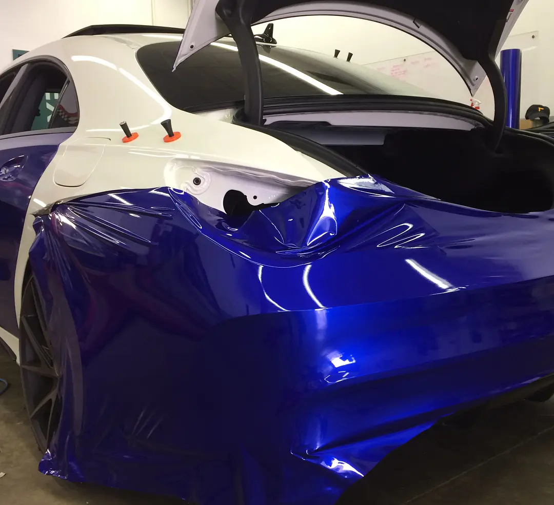 Deep blue wrap film laid loose over the rear quarter of a Mercedes part way through installation, the panel behind it still factory white