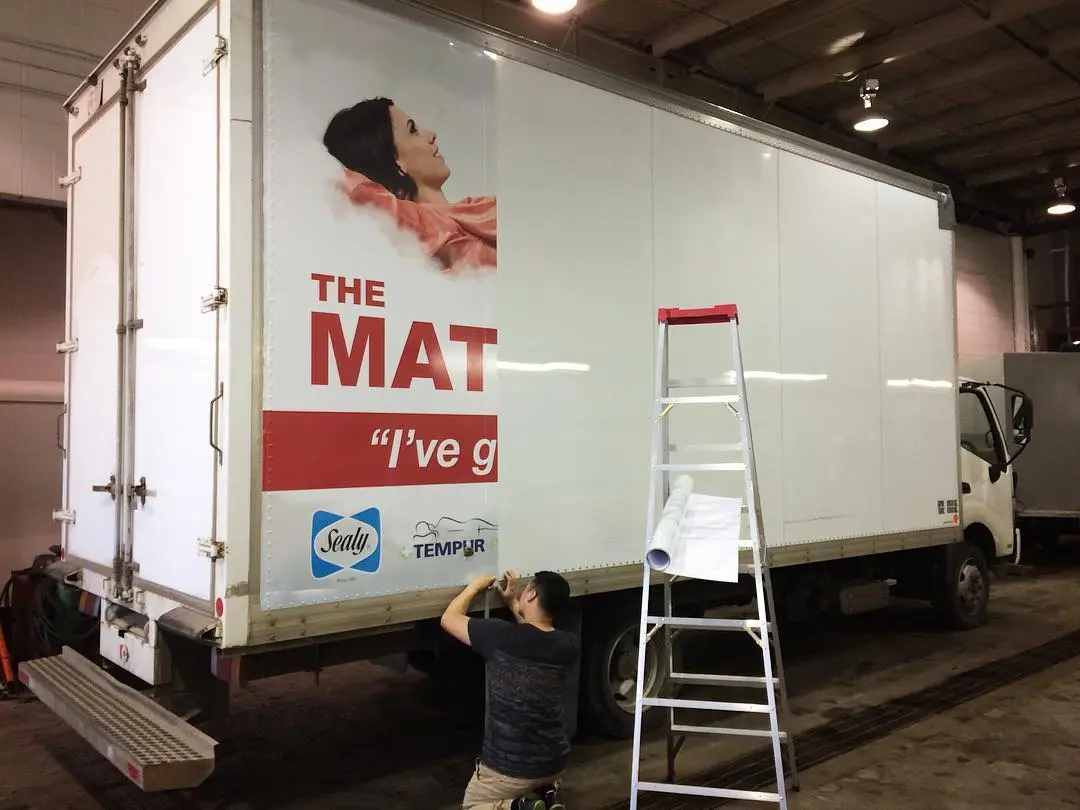 An installer on a step ladder squeegeeing a large format printed graphic onto the side of a box truck