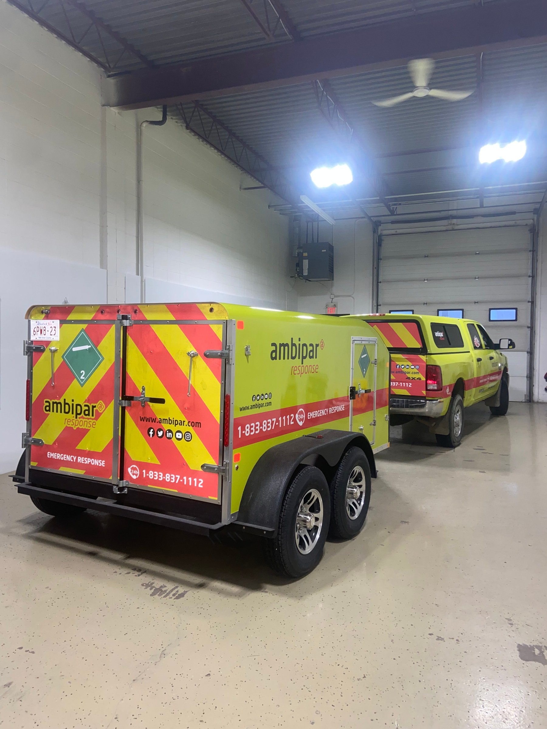 Two Ambipar emergency response vehicles and a matching trailer lined up in the shop, all carrying the same yellow and red chevron livery
