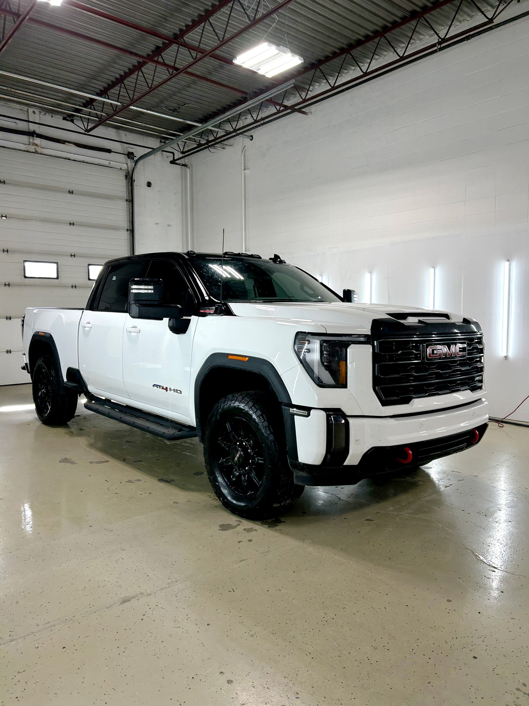 A white GMC Sierra HD pickup finished in a full wrap, photographed front three quarter in a Choice Graphics shop bay