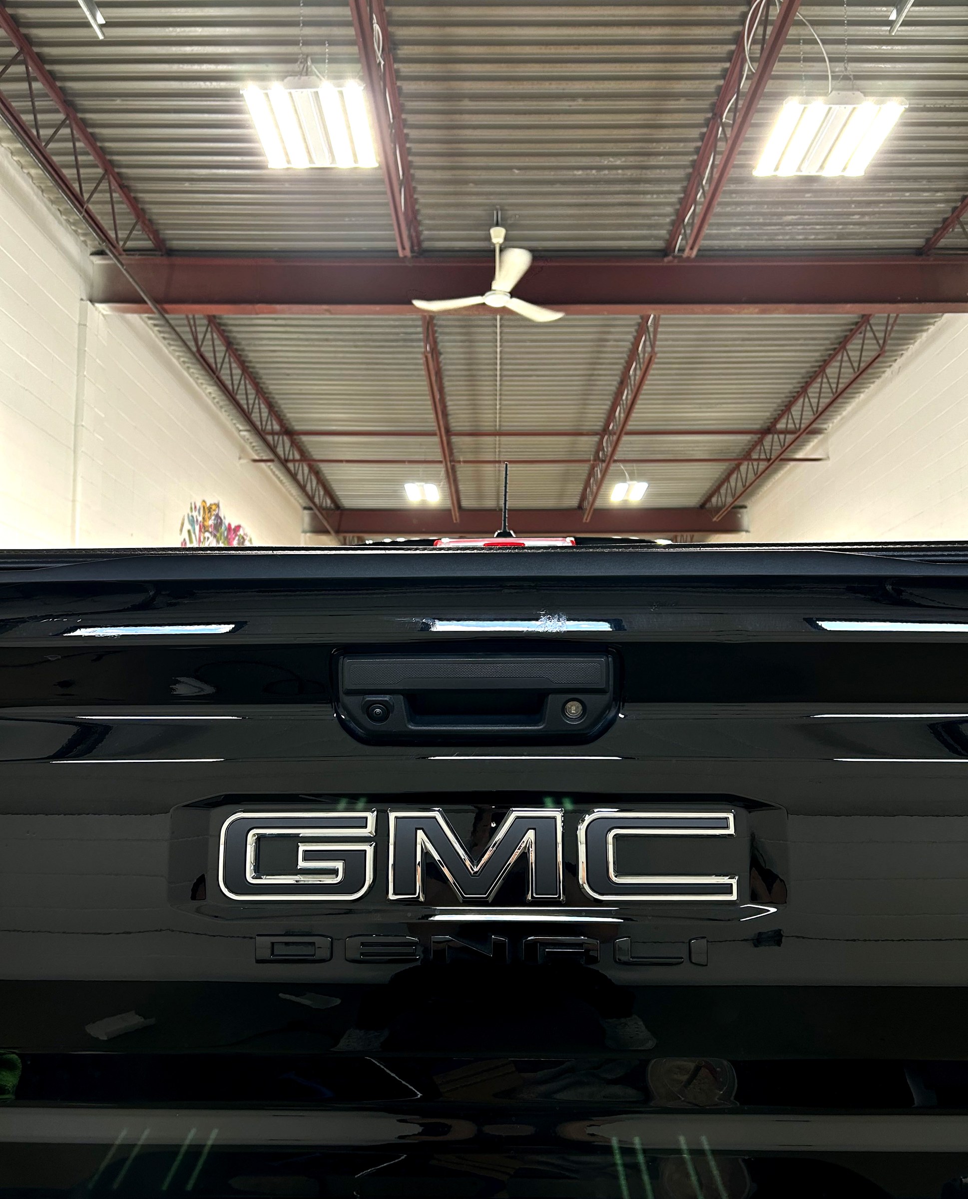 Close up of a wrapped GMC tailgate with the badge blacked out, showing the film worked cleanly around the badge and body line