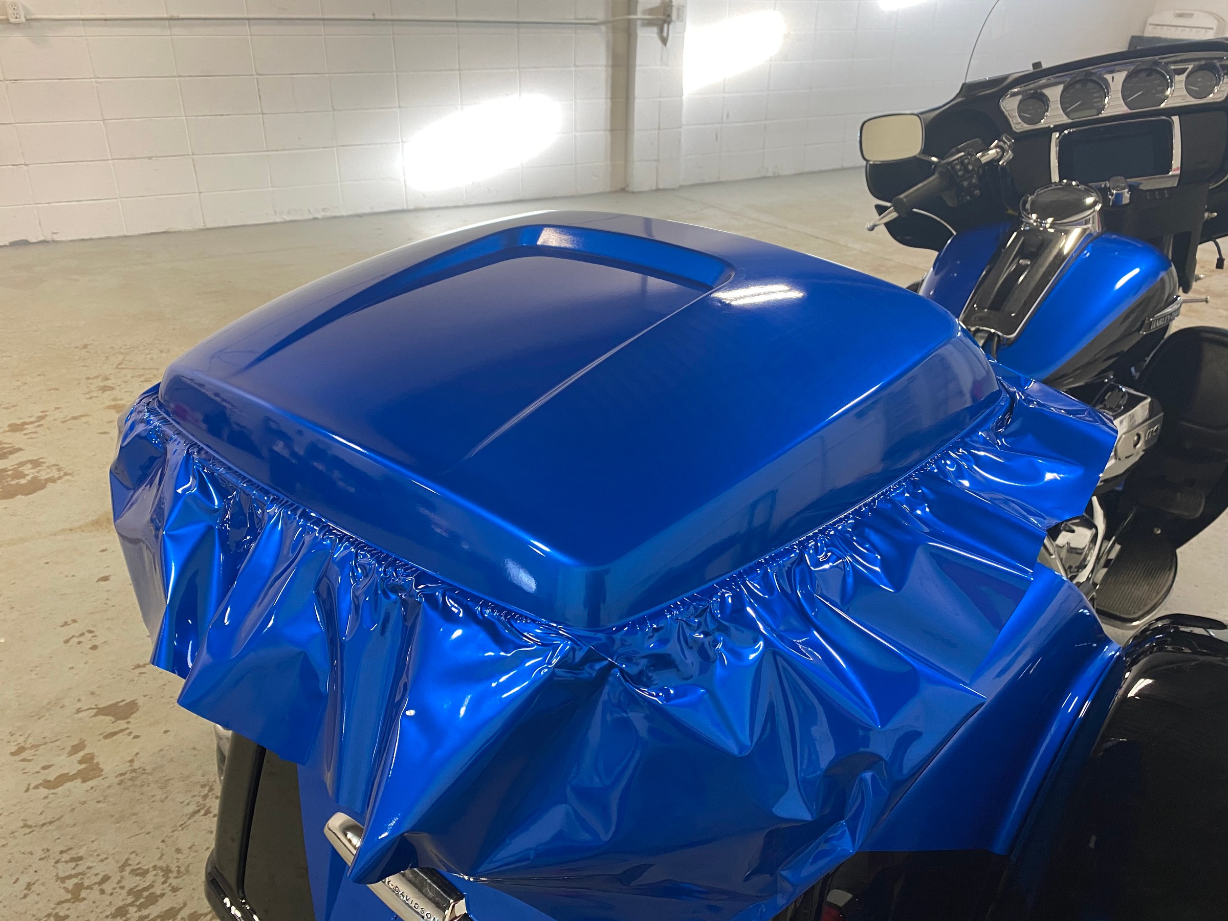 Blue wrap film laid loose over a motorcycle body panel part way through installation, before it is heated and squeegeed into the contours