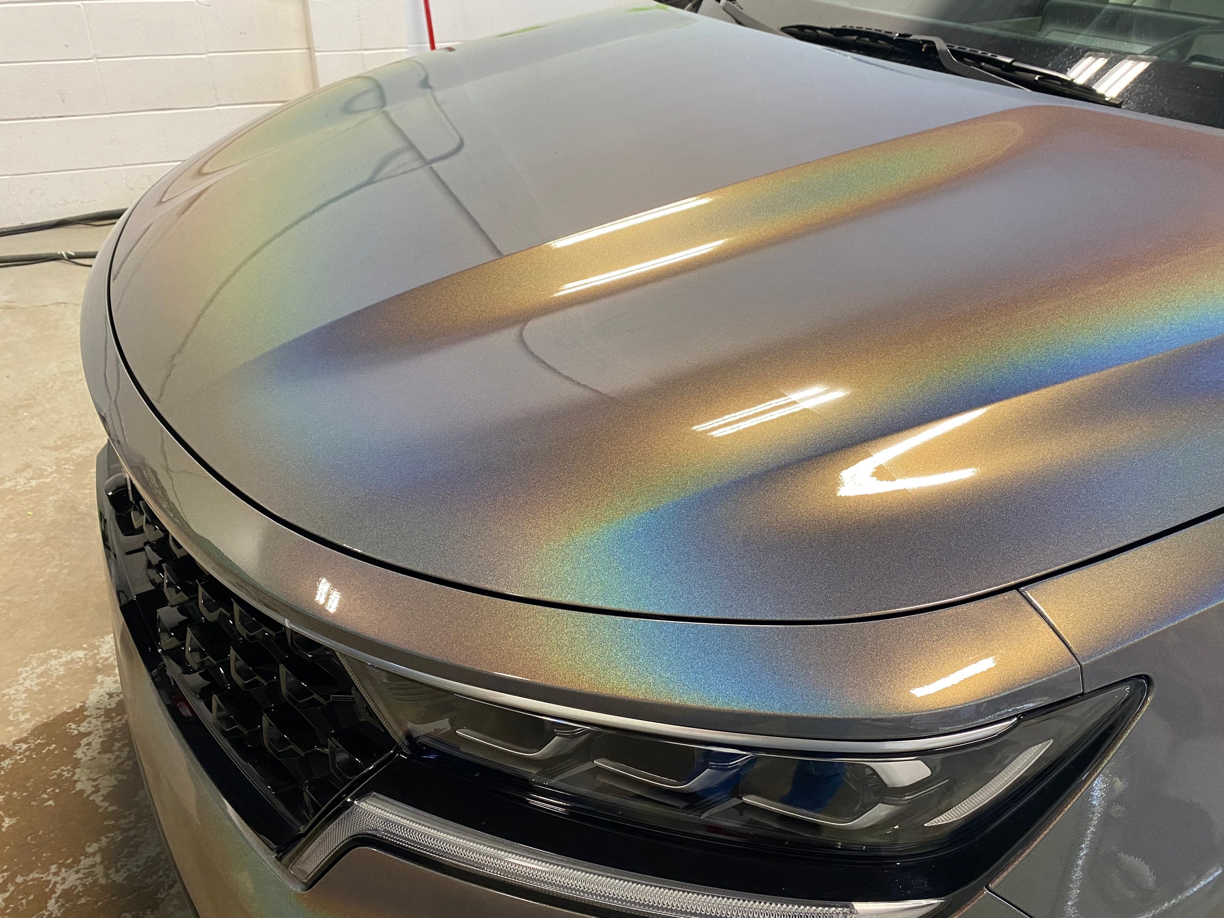 Close up of a vehicle hood wrapped in a colour shift film, the surface reading grey, gold, and green depending on the viewing angle