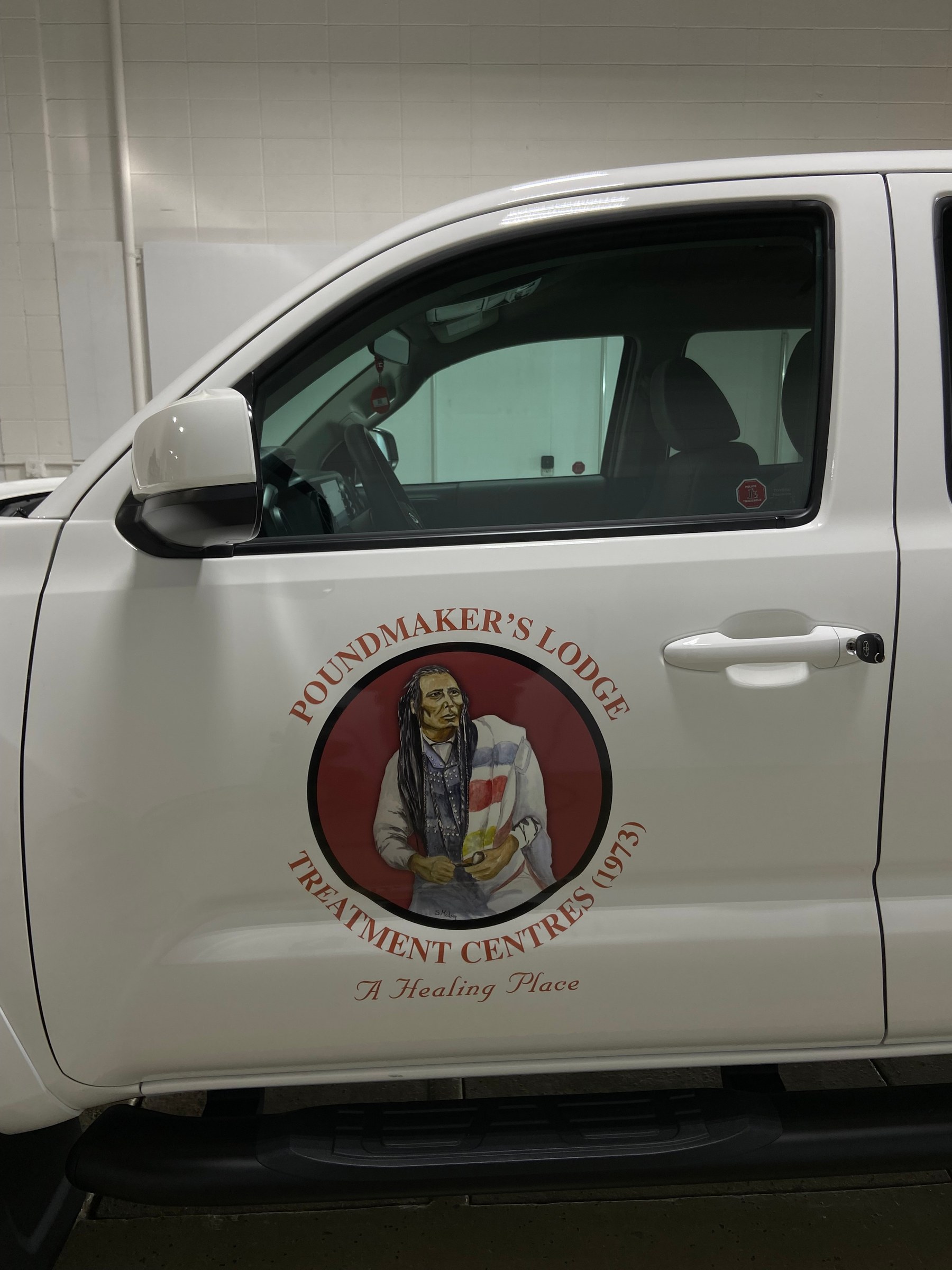 Close up of a printed circular Poundmaker's Lodge Treatment Centres door decal applied to the front door of a white pickup