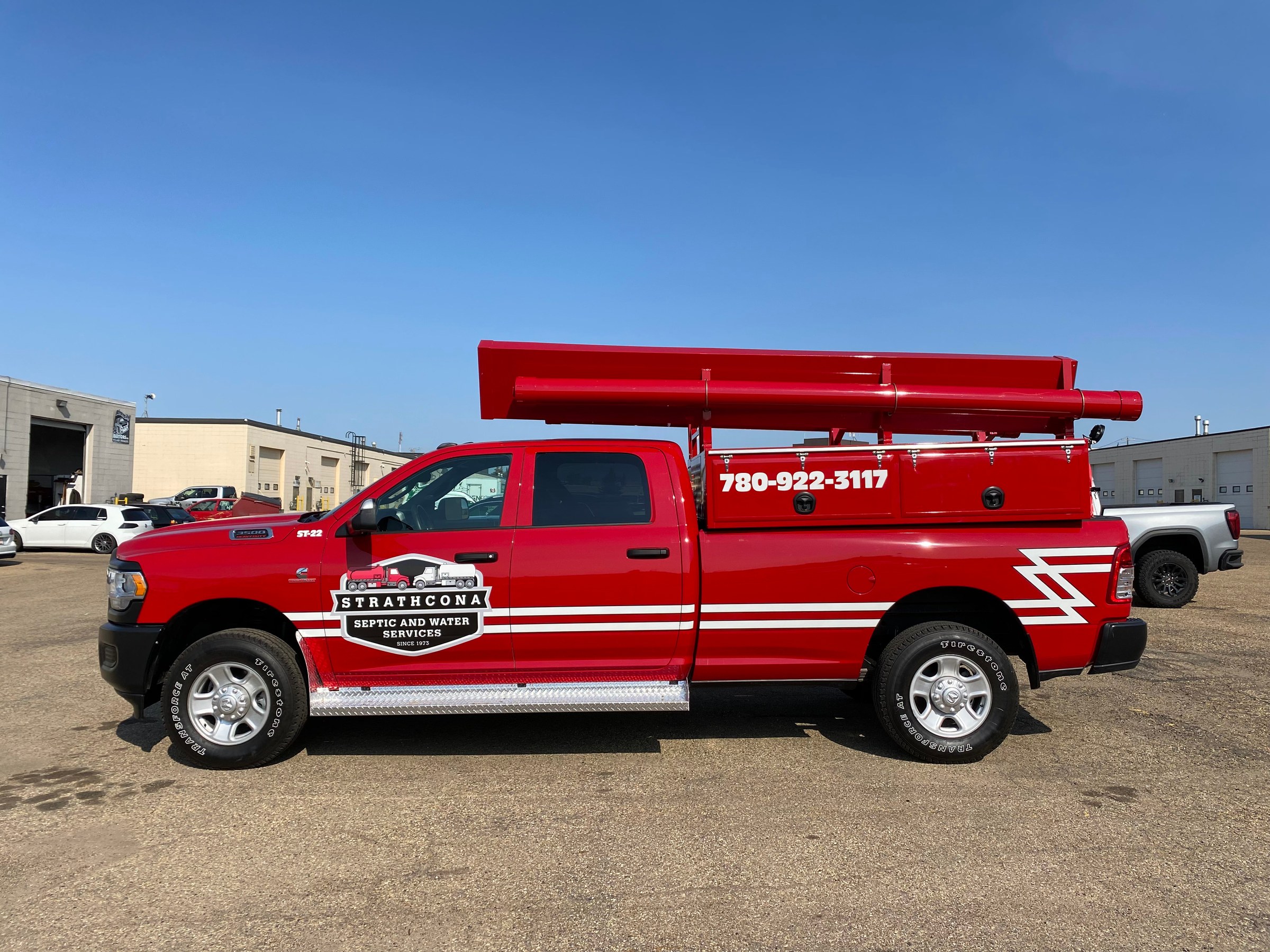 A Strathcona Septic and Water red service truck with white graphics and phone number, loaded with pipe racks and photographed outdoors