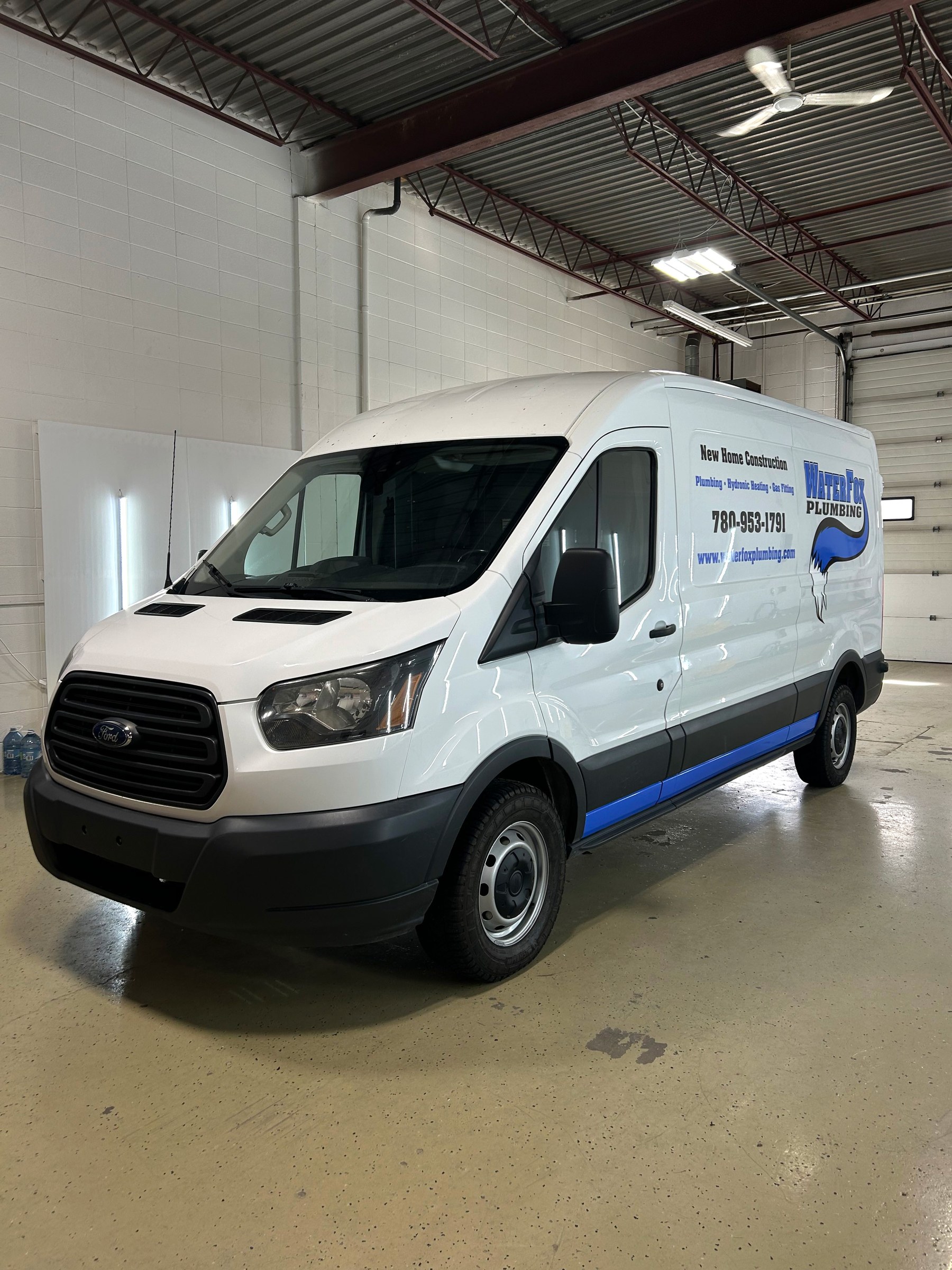 Side view of a WaterFox Plumbing Ford Transit cargo van in a white wrap with a blue wave graphic and contact details